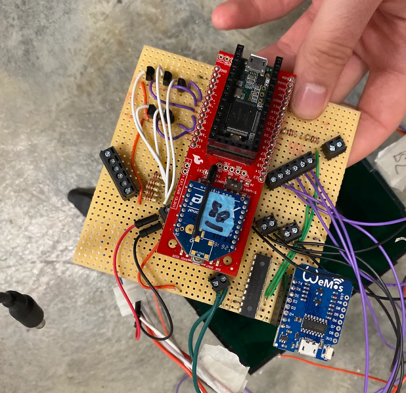 Holding one of the hand-soldered circuit boards, a microcontroller and wiring on perfboard