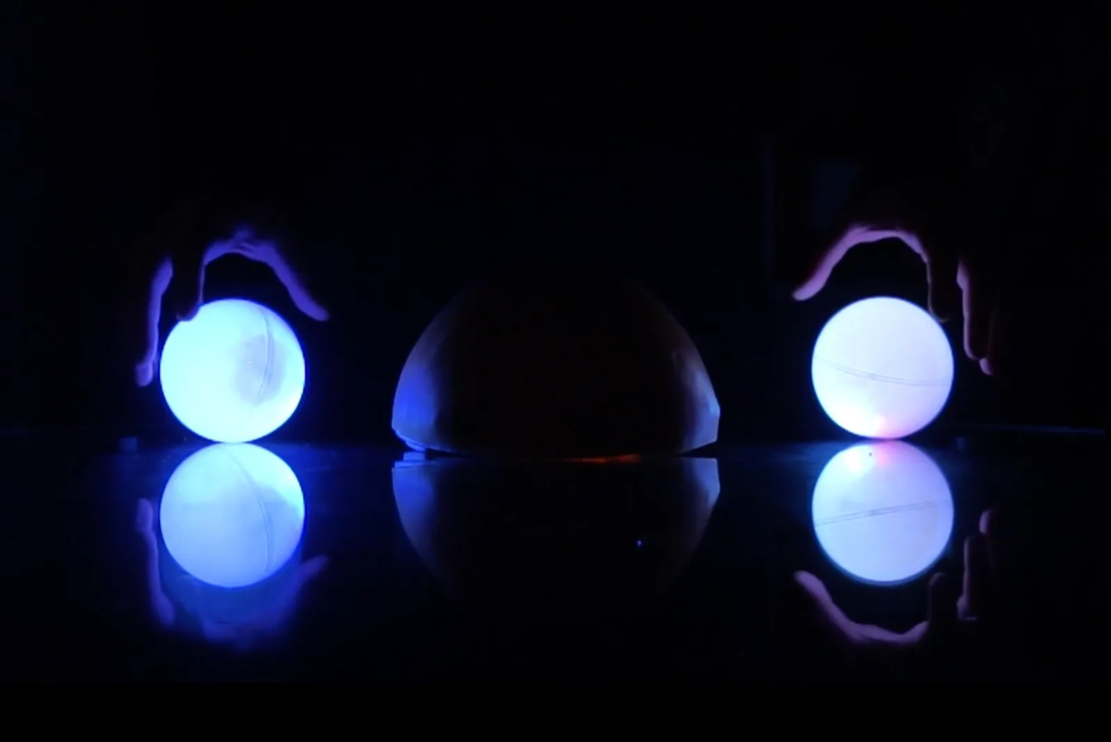 Two glowing blue domes on a black table, each above a pool of its own light